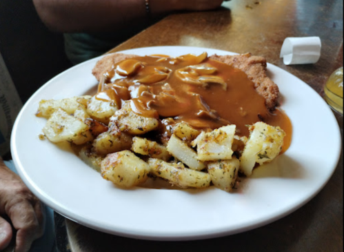 A plate of breaded chicken with mushroom gravy, served with seasoned roasted potatoes.