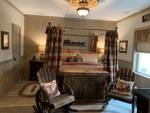 Cozy bedroom with a wooden bed, plaid curtains, rustic decor, and two wooden chairs in a warm, inviting atmosphere.