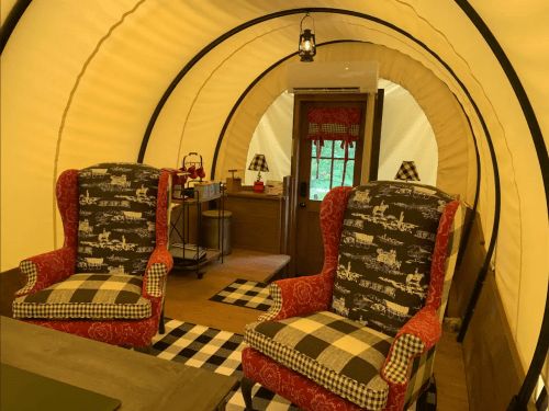 Cozy interior of a glamping tent featuring two patterned chairs, a wooden table, and warm lighting.