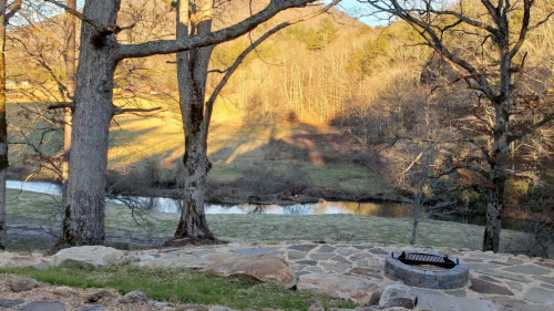 A serene landscape featuring a river, trees, and a stone patio, illuminated by warm sunlight in a tranquil setting.