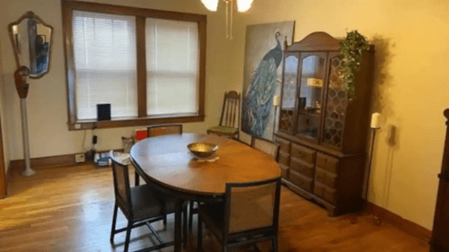 A cozy dining room featuring a round wooden table, chairs, a cabinet, and a peacock painting on the wall.