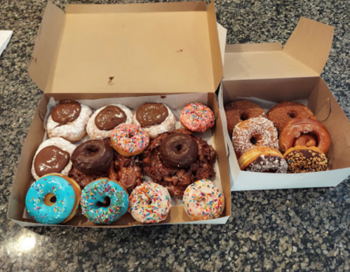 A box of assorted donuts, including chocolate, glazed, and colorful sprinkles, on a granite countertop.