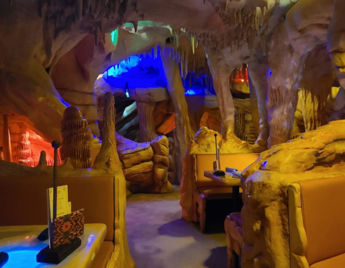 A dimly lit cave-themed restaurant interior with colorful lights and unique rock formations.