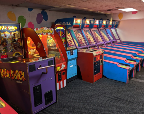A colorful arcade with various games, including a popcorn machine and several pinball machines, in a festive setting.