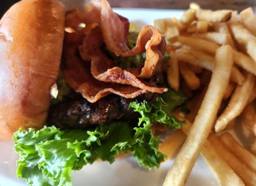 A juicy burger with bacon and lettuce, served with a side of golden French fries on a white plate.
