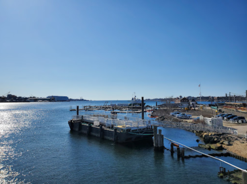 A calm harbor scene with boats, a clear blue sky, and a dock extending into the water.