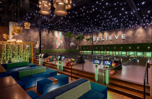 A vibrant bowling alley with green seating, starry lights, and a "BELIEVE" mural on the wall.