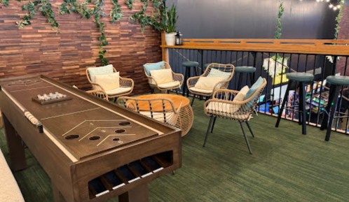 A cozy lounge area featuring a shuffleboard table, stylish chairs, and greenery against a wooden wall.