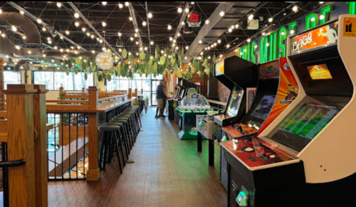 A vibrant arcade with vintage games, bar seating, and string lights in a lively atmosphere.