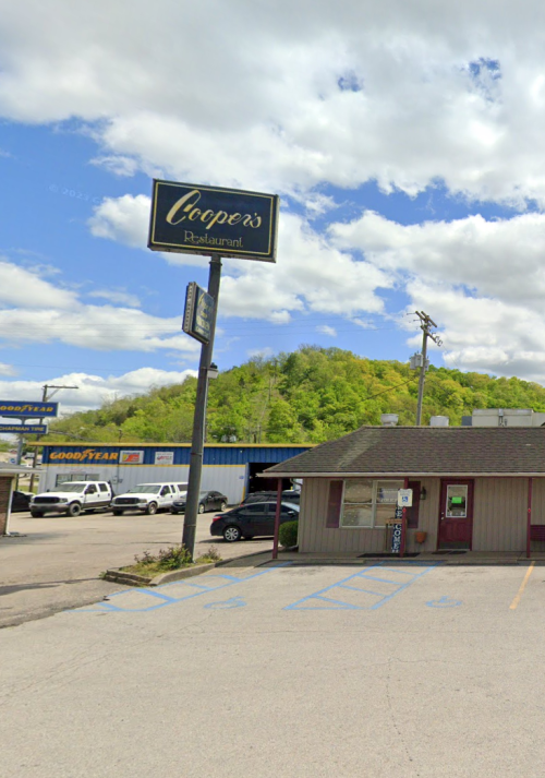 A restaurant named "Cooper's" with a sign, surrounded by greenery and a parking lot under a partly cloudy sky.