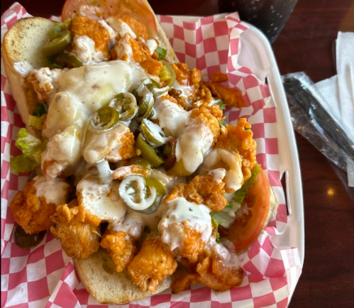 A sandwich filled with crispy chicken, lettuce, jalapeños, and drizzled with sauce, served in a checkered basket.