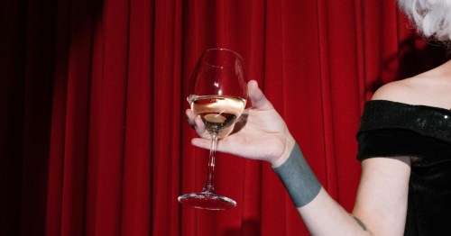 A person in a black dress holding a glass of wine against red velvet curtains at a New Orleans speakeasy.
