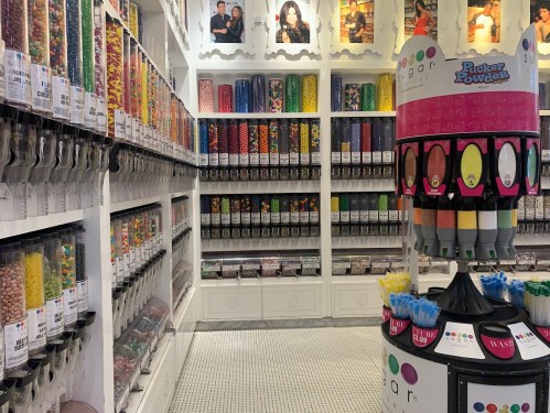 A colorful candy store interior with various candy bins and a display of candy containers in the center.