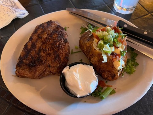 A plate with a grilled steak and a loaded baked potato topped with green onions, bacon, and sour cream.