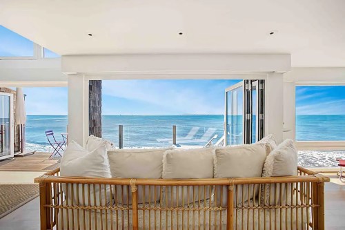 Cozy beachside living room with a rattan sofa, open to a stunning ocean view and bright blue sky.