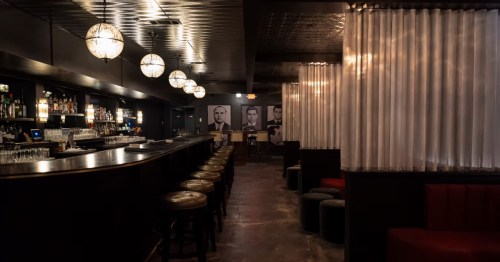 The interior of a Texas speakeasy with dim lighting, large booths, and a long bar.