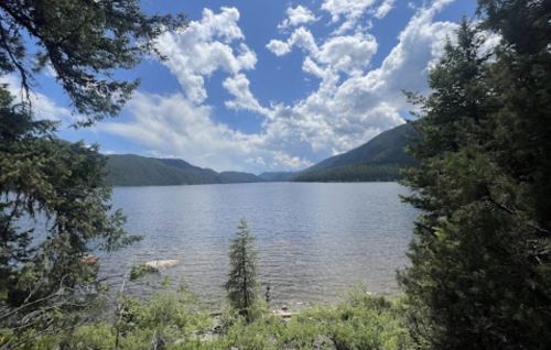 A serene lake surrounded by mountains and trees under a partly cloudy sky.