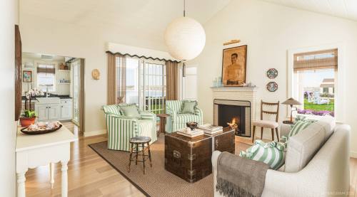 Bright, airy living room with striped chairs, a cozy sofa, a fireplace, and a large round pendant light.