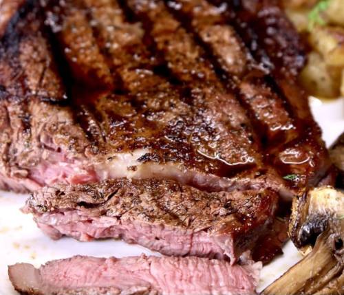 Close-up of a perfectly cooked steak, showcasing a juicy, pink interior and charred exterior, served with roasted potatoes.