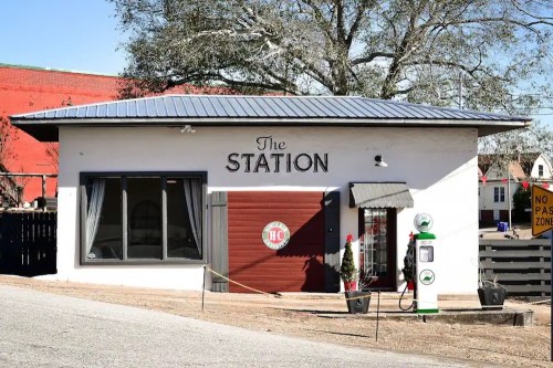 A small, white building with a sign reading "The Station," featuring a vintage gas pump outside.