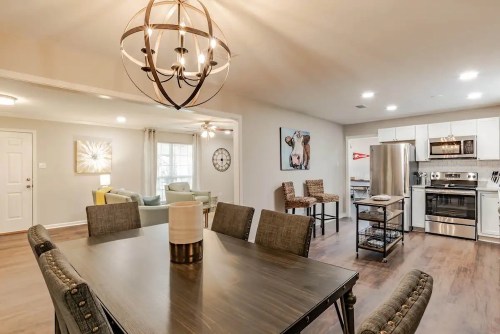 Modern dining area with a large table, stylish lighting, and an open kitchen featuring stainless steel appliances.