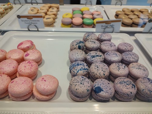 A display of colorful macarons in various flavors, including pink strawberry cheesecake and purple blueberry.