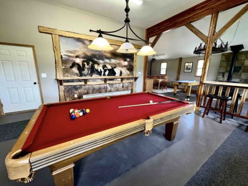 A cozy game room featuring a red pool table, wooden beams, and a mural of cows on the wall.