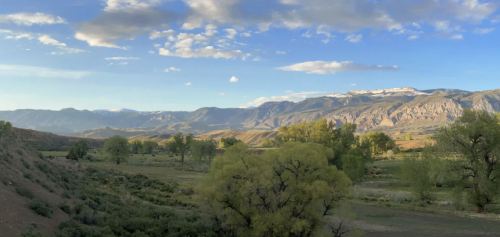 A scenic landscape featuring mountains, green trees, and a blue sky with scattered clouds.