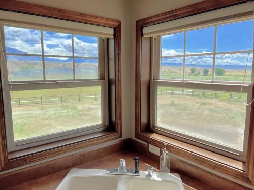 View from a room with two windows, showcasing a scenic landscape of fields and mountains under a blue sky.