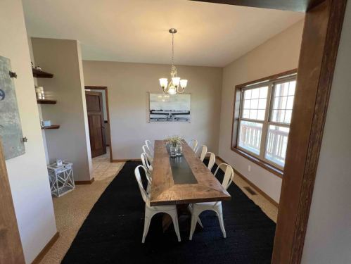 A modern dining room featuring a wooden table, white chairs, a chandelier, and large windows with natural light.