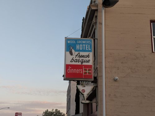 Sign for Wool Growers Hotel featuring "French Basque" and "Dinners" in bold letters against a clear sky.