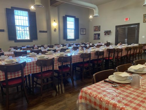 A spacious dining room with a long table set with checkered tablecloths, plates, and utensils, ready for a meal.