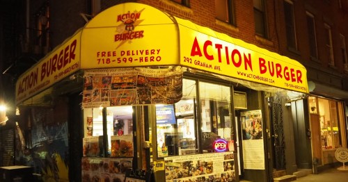 A brightly lit burger restaurant with a yellow awning displaying "Action Burger" and a welcoming "Open" sign.