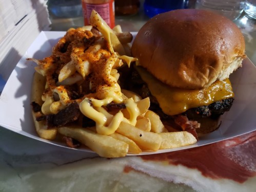 A plate featuring a cheeseburger with a soft bun and melted cheese, alongside loaded fries topped with cheese and seasoning.