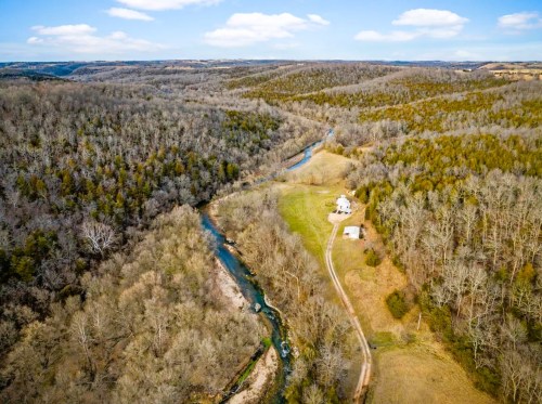 Aerial view of a winding river through a wooded landscape with a small house and open fields.