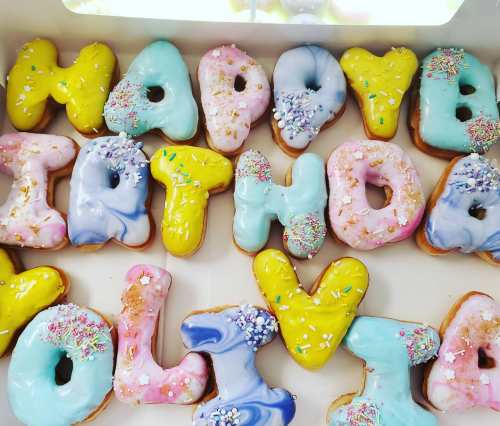 Colorful birthday donuts arranged to spell "Happy Birthday Olivia" with sprinkles on top.