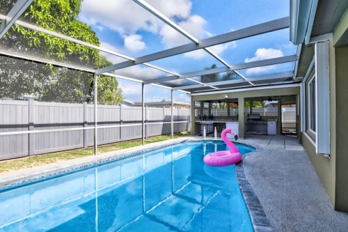 A sunny backyard with a clear pool, a pink flamingo float, and a screened patio area.