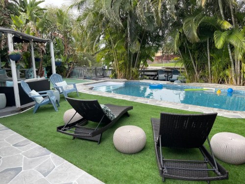 A serene backyard with a pool, lounge chairs, and tropical plants, creating a relaxing outdoor space.