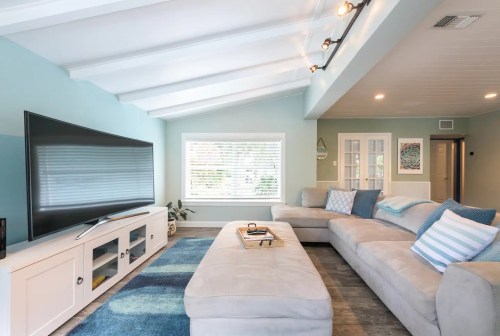 Bright living room with a large TV, light blue walls, a cozy sectional sofa, and a stylish area rug.