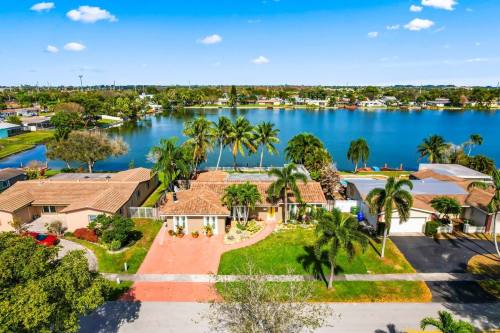 Aerial view of a waterfront neighborhood with palm trees, houses, and a serene lake under a clear blue sky.