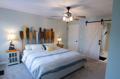 Cozy bedroom with a bed, colorful paddle wall art, a lamp, and a sliding barn door leading to a bathroom.