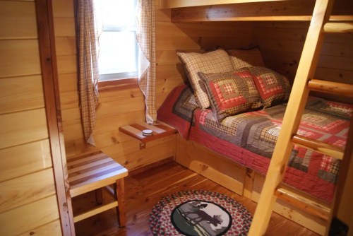 Cozy wooden cabin interior featuring a bed with a quilt, a small table, and a decorative rug.