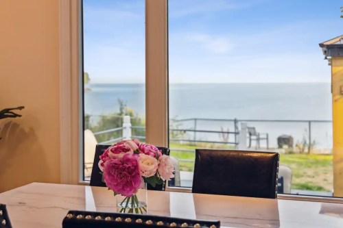 A dining table with a flower vase, overlooking a serene lake view through large windows.
