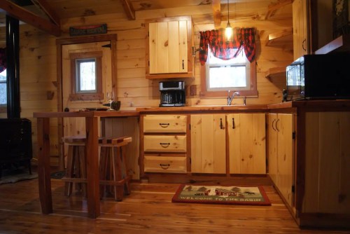 Cozy wooden kitchen with a small table, stools, and rustic cabinets, featuring warm lighting and a welcoming atmosphere.