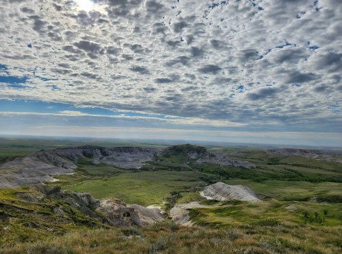 A vast landscape with rolling hills, green valleys, and a dramatic sky filled with clouds.