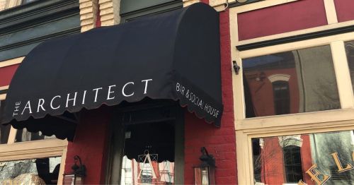 A black awning with the text "THE ARCHITECT" above a restaurant entrance, featuring red and cream-colored walls.
