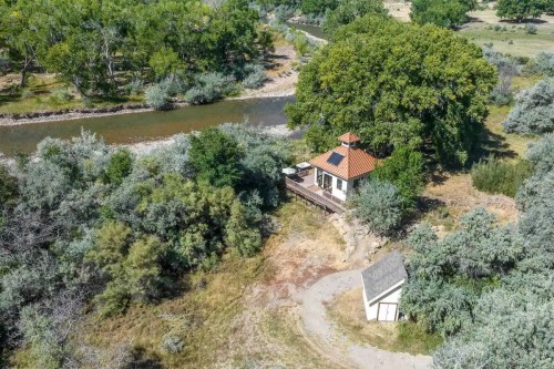 Aerial view of a small house by a river, surrounded by greenery and trees, with a shed nearby.