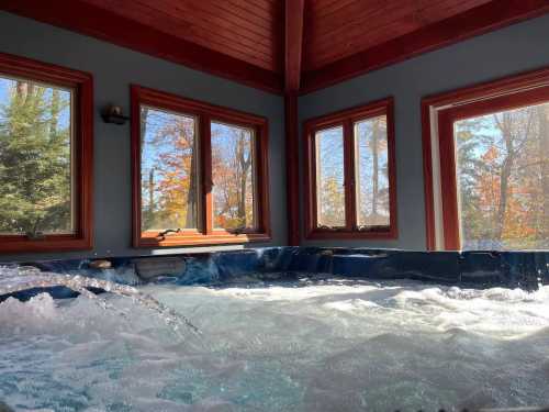 A cozy indoor hot tub surrounded by large windows showcasing autumn foliage outside.