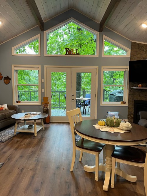 Cozy living space with large windows, a dining table, and a view of greenery outside. Decorated for fall.