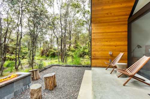 A cozy outdoor space with wooden chairs, a fire pit, and a lush forest backdrop.